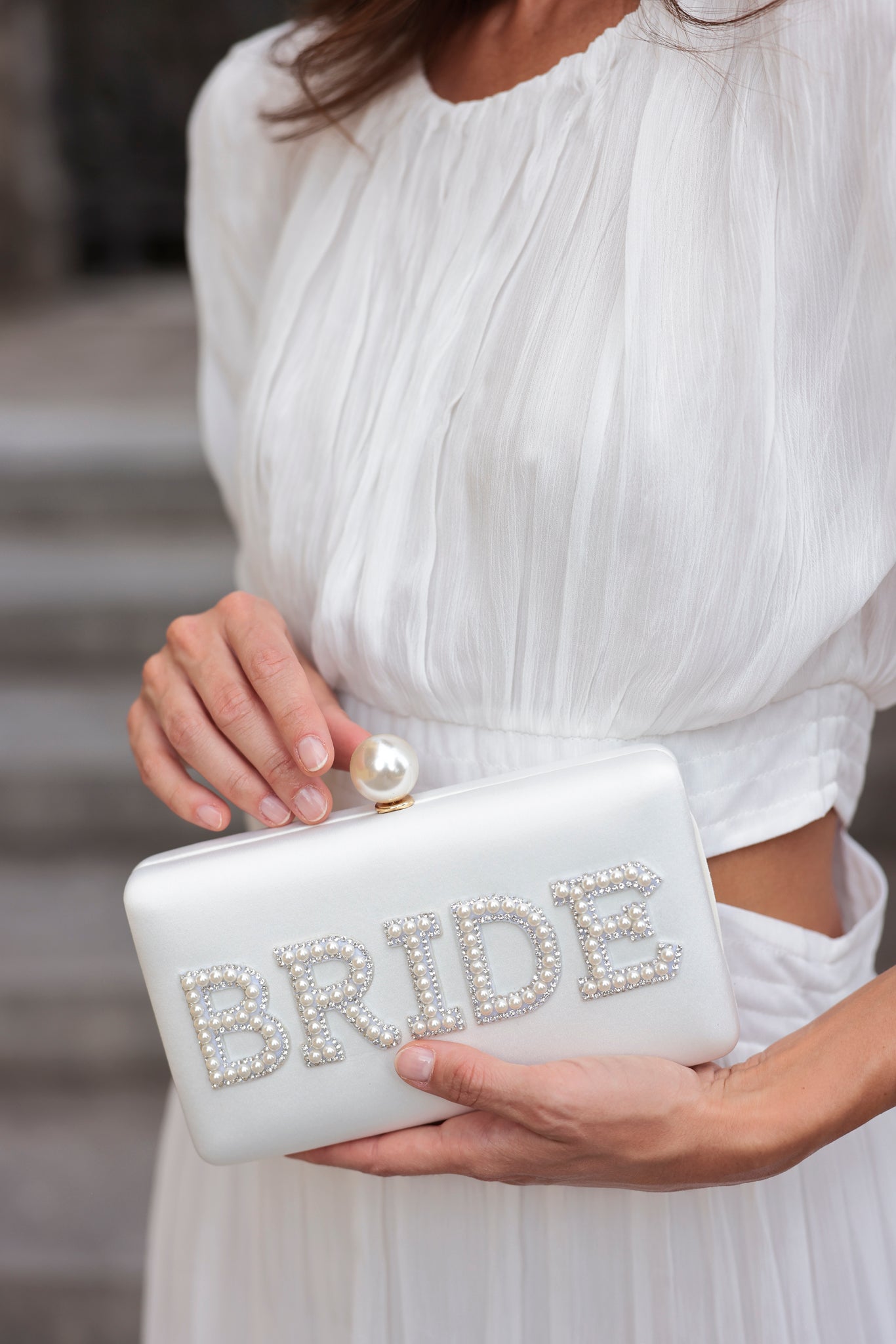 Bring your bridal celebrations wherever you go with Shiraleah's "Bride" Pearl Minaudiere. This classic white purse features the word "Bride" embroidered in chic faux pearls with a faux pearl top closure. You can carry it like a clutch or use the detachable cross-body chain for some extra versatilaty in your style. Pair with other items from Shiraleah's Hitched collection to complete your look!